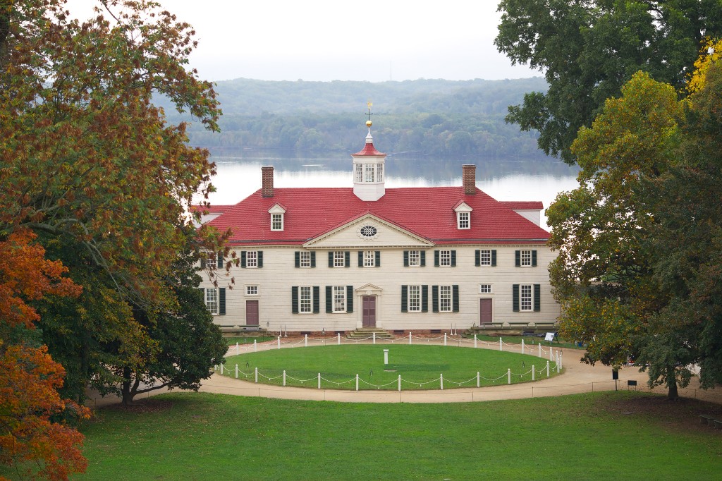 Mount Vernon mansion with red roof overlooking the Potomac River, framed by autumn trees